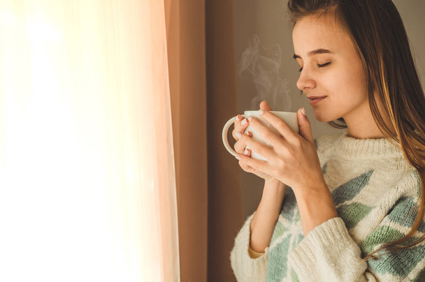 Pencerenin yanında bir fincan sıcak içecek olan kadın. Pencereye bakıp çay içiyorum. Çayile günaydın - Fotoğraf, Görsel