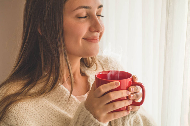 Жінка з чашкою гарячого напою біля вікна. Дивлячись на вікно і п'ючи чай. Доброго ранку з чаєм
 - Фото, зображення