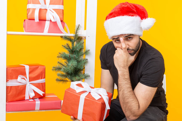 Jeune homme beau dans un chapeau de Père Noël tient cadeaux de félicitations à côté d'un arbre de Noël. Concept de vacances de Noël et du nouvel an
. - Photo, image