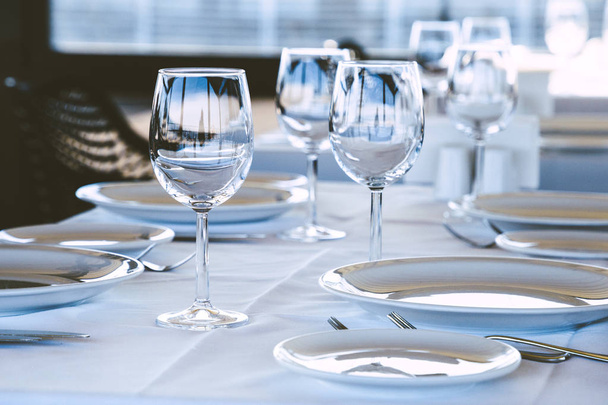 Table setting in restaurant. Empty wine glasses, plates, forks, knifes on the tablecloth. Elegant restaurant interior. - Photo, Image