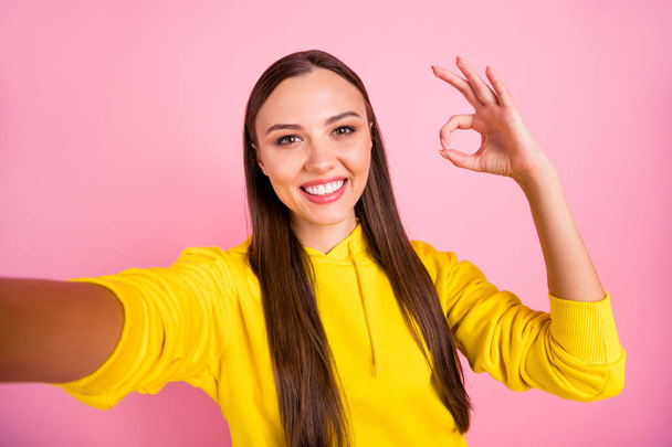 Self portrait of cheerful cute pretty sweet lovely fascinating girlfriend brunette haired showing you ok sign taking selfie wearing yellow sweater while isolated over pink pastel color background - Valokuva, kuva