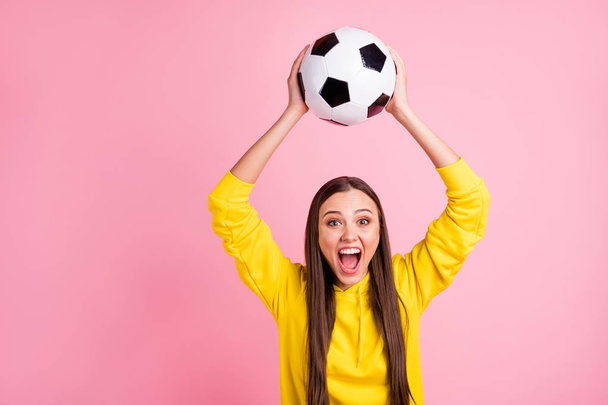 Photo of charming cute overjoyed girlfriend holding soccer ball above her head wearing yellow sweater while isolated over pink pastel color background - Фото, изображение