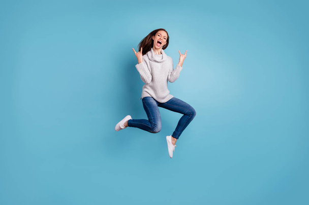 Full length photo of cheerful content youth jump show horns signs jump feel rejoice have weekend party wear white pullover denim jeans sneakers isolated over blue color background - Foto, Bild