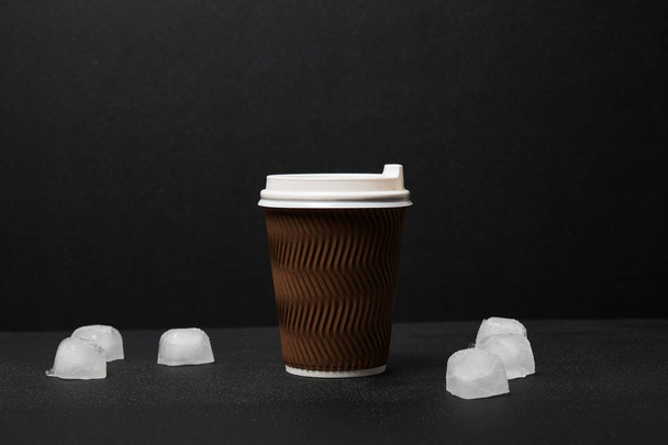 Крупный план одноразовой чашки кофе и кубиков льда на черном фоне
 - Фото, изображение