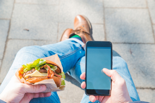 man holding burger and mobile phone. white screen - Photo, image