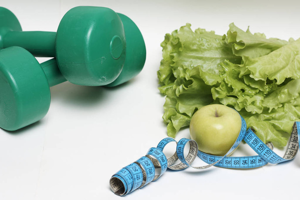 Salatblatt und Apfel mit blauem Maßband und Hanteln isoliert auf weißem Hintergrund, Diätkonzept. - Foto, Bild