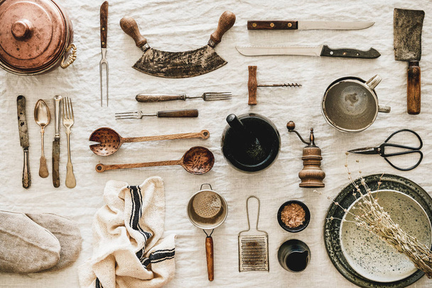 Flat-lay of various kitchen utensils, rustic tablewear, plates, dishes, glasswear, pan, scissors, corkscrew, textile for cooking over white linen tablecloth background, top view. Seasonal cooking - Foto, Imagem