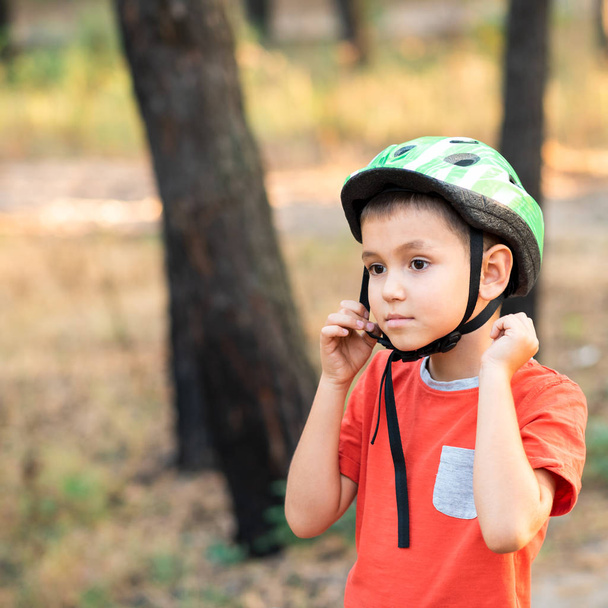 A boy puts a green helmet on his head. - Foto, Imagen