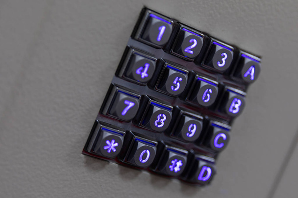 Μαύρο μεταλλικό κουμπί με αριθμούς μπλε λαμπερά φώτα, συμπεριλαμβανομένων των αριθμών πινακίδα και αστερίσκο, A B C γράμματα σε γκρίζα αφηρημένη επιφάνεια, διαγώνια προβολή. - Φωτογραφία, εικόνα