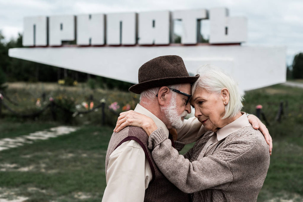 PRIPYAT, UKRAINE - AUGUST 15, 2019: selective focus of senior couple hugging near monument with pripyat letters  - Foto, afbeelding