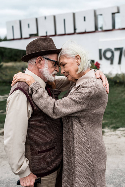 PRIPYAT, UCRANIA - 15 de agosto de 2019: enfoque selectivo de la pareja jubilada abrazándose cerca del monumento con letras pripyat
  - Foto, Imagen