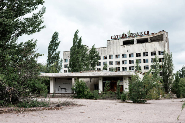 PRIPYAT, UKRAINE - AUGUST 15, 2019: building with hotel polissya lettering near trees in chernobyl  - Fotografie, Obrázek