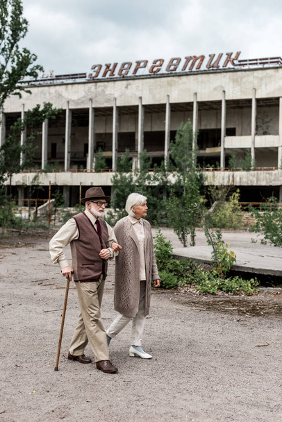 PRIPYAT, UKRAINE - AUGUST 15, 2019: senior couple walking near building with energetic lettering in chernobyl  - Foto, Bild