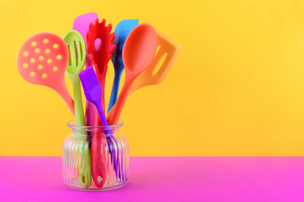 bright multi colored kitchen utensils on yellow and purple background with copy space - Foto, afbeelding