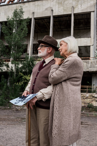PRIPYAT, UKRAINE - AUGUST 15, 2019: retired man and woman holding black and white photo near building - Foto, Imagen