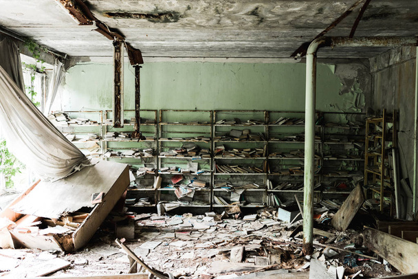 PRIPYAT, UKRAINE - AUGUST 15, 2019: dirty and abandoned library with books on floor in school  - Foto, imagen