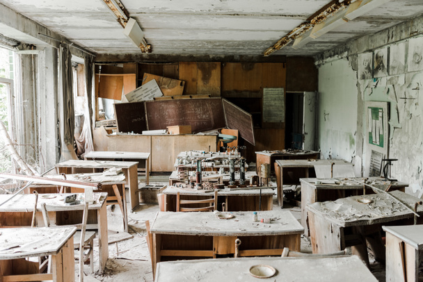 Verlassenes und gruseliges Klassenzimmer mit schmutzigen Tischen und Kreidetafel in der Schule  - Foto, Bild
