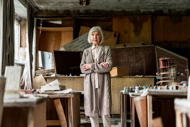 selektivní zaměření ženy v důchodu stojící za zkříženýma rukama u špinavých stolů  - Fotografie, Obrázek