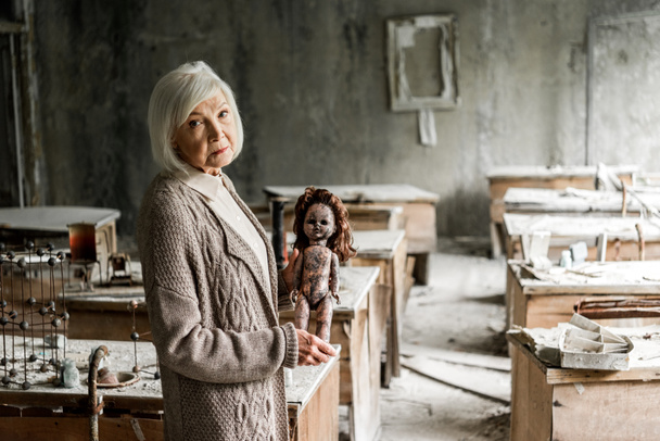 汚れた赤ちゃんの人形を保持する灰色の髪を持つ引退した女性の選択的な焦点  - 写真・画像