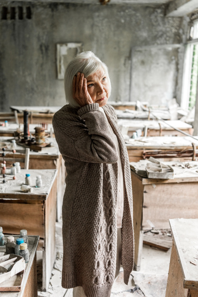 Rentnerin berührt graue Haare und steht in schmutzigem Klassenzimmer  - Foto, Bild