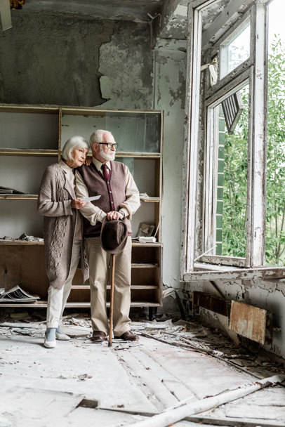 manželé v důchodu s pohledem na okno, když stáli v poškozené učebně  - Fotografie, Obrázek