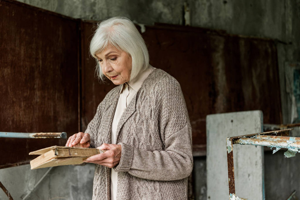 PRIPYAT, UKRAINE - AUGUST 15, 2019: senior woman with grey hair holding book in hands - Foto, Imagen