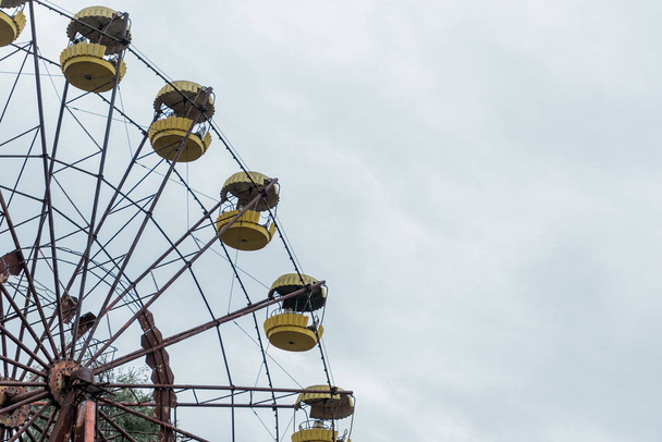 PRIPYAT, UKRAINE - AUGUST 15, 2019: abandoned and rusty ferris wheel in amusement park against blue sky with clouds  - Foto, imagen