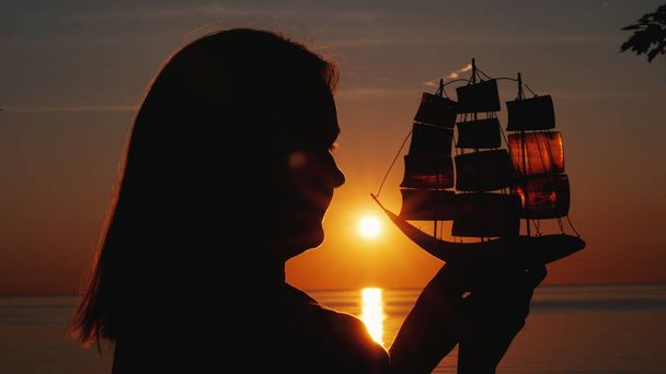 Profil d'une femme avec un voilier jouet contre le soleil couchant
 - Photo, image