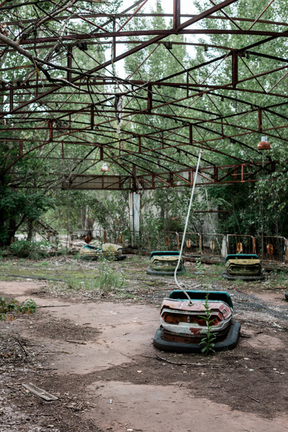 PRIPYAT, UKRAINE - AUGUST 15, 2019: bumper cars in abandoned amusement park near trees - Fotó, kép