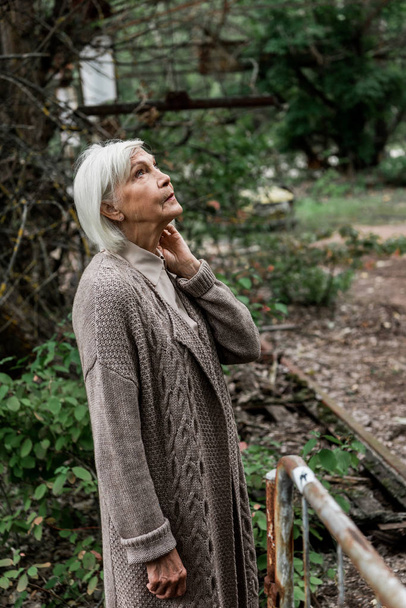 ηλικιωμένη γυναίκα με γκρίζα μαλλιά που στέκονται σε εγκαταλελειμμένο πάρκο στο Τσερνομπίλ  - Φωτογραφία, εικόνα