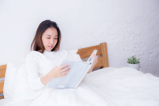Mujer asiática leyendo un libro y sonriendo en el dormitorio. estilo de vida con
 - Foto, imagen