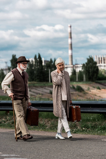 PRIPYAT, UKRAINE - AUGUST 15, 2019: senior man and woman walking with luggage near chernobyl nuclear power plant  - Fotoğraf, Görsel