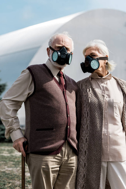 PRIPYAT, UCRAINA - 15 AGOSTO 2019: marito e moglie anziani in maschere protettive in piedi vicino al reattore di Chernobyl abbandonato
  - Foto, immagini