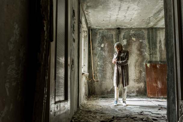 грустная старшая женщина, стоящая в пустой и грязной комнате
  - Фото, изображение