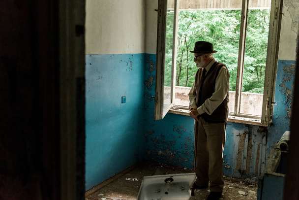 λυπημένος ανώτερος άνθρωπος στέκεται σε κατεστραμμένο δωμάτιο  - Φωτογραφία, εικόνα