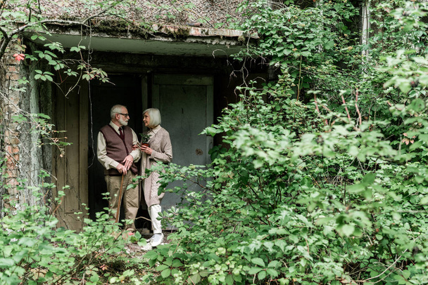 starší muž, který se dívá na důchodce s rostlině v hrnci, zatímco stojí blízko domu  - Fotografie, Obrázek