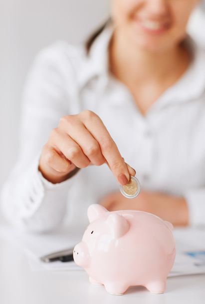 Woman hand putting coin into small piggy bank - Fotó, kép