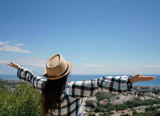 帽子をかぶった魅力的な女の子の観光客は、彼女の腕を広げて広げ、旅、自由を楽しんで、山の上に立っています - 写真・画像