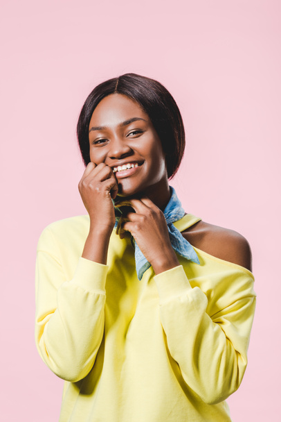 smiling african american woman in yellow pullover and scarf looking at camera isolated on pink  - Foto, Bild