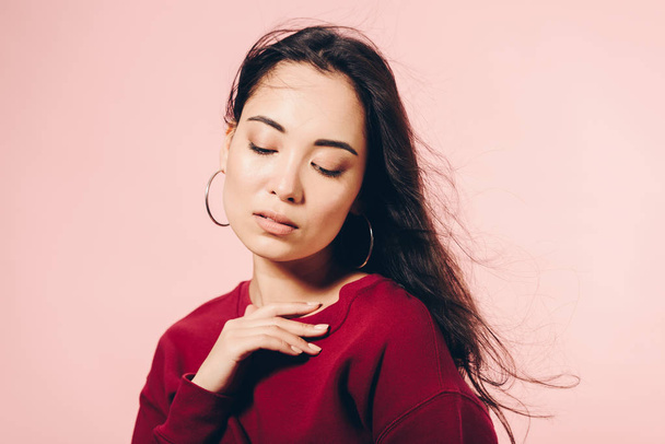 attractive asian woman in red sweater with closed eyes isolated on pink  - Zdjęcie, obraz