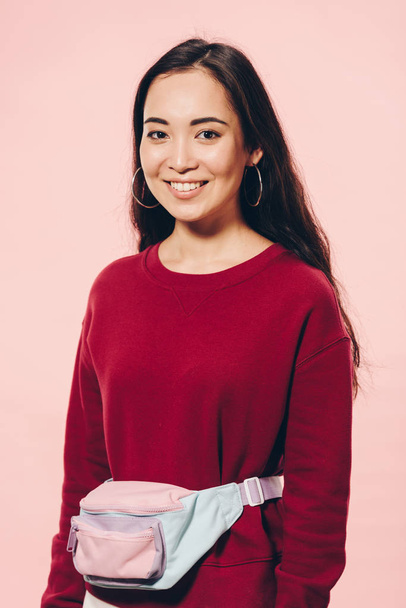 attractive asian woman in red sweater smiling isolated on pink  - Fotografie, Obrázek