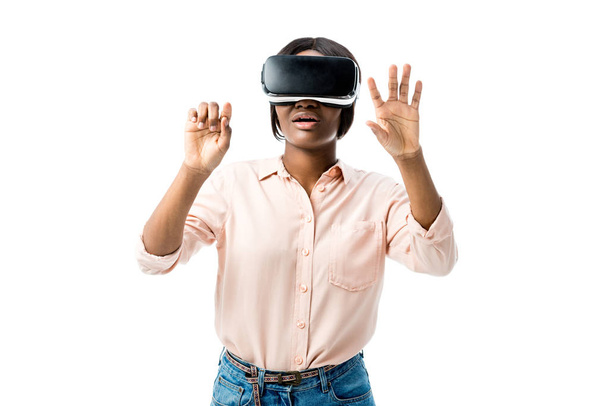 geschokt Afrikaans amerikaanse vrouw in shirt met virtual reality headset tonen handen geïsoleerd op wit  - Foto, afbeelding