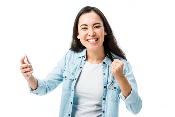 aantrekkelijke aziatische vrouw in denim shirt tonen ja gebaar en houden smartphone geïsoleerd op wit  - Foto, afbeelding