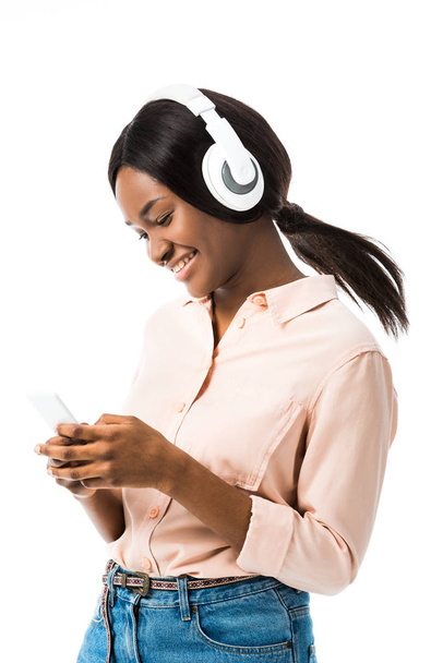 sonriente mujer afroamericana con auriculares sosteniendo teléfono inteligente aislado en blanco
  - Foto, Imagen