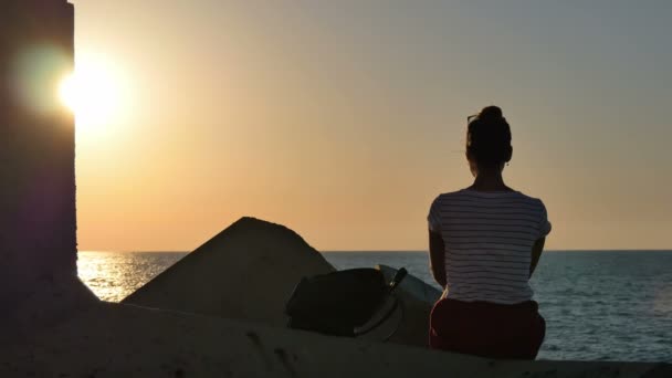 Jonge vrouw zittend op de rotsen en kijken naar de zonsondergang zee - Video