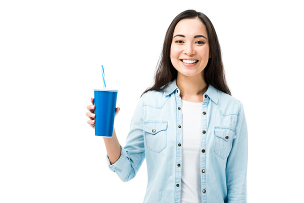 приваблива і усміхнена азіатська жінка в джинсовій сорочці, що тримає пластикову чашку ізольовано на білому
  - Фото, зображення