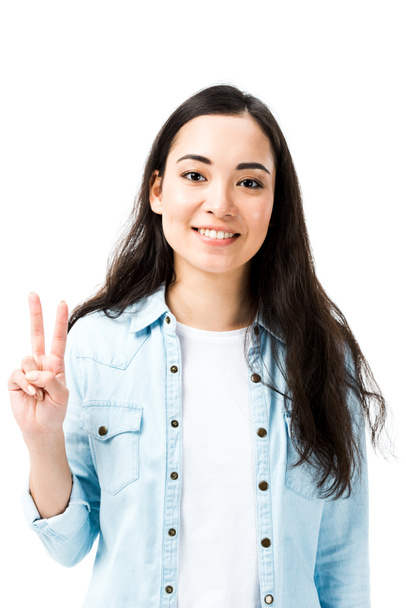 atractivo y sonriente asiático mujer en denim camisa mostrando paz signo aislado en blanco
  - Foto, imagen