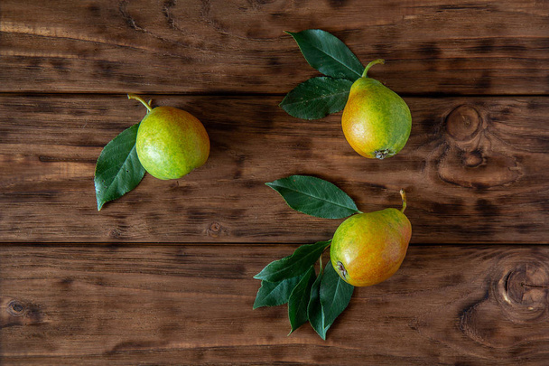 Three fresh pears with leaves lie on a wooden table - Фото, изображение