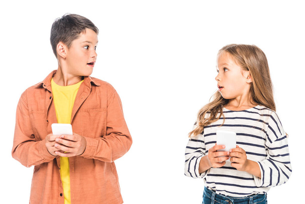 two shocked kids using smartphones and looking at each other isolated on white - Foto, Imagem