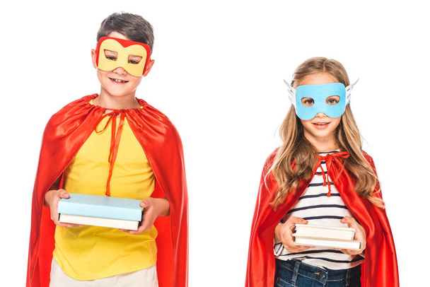 front view of two smiling kids in masks and hero cloaks holding books isolated on white - Photo, Image